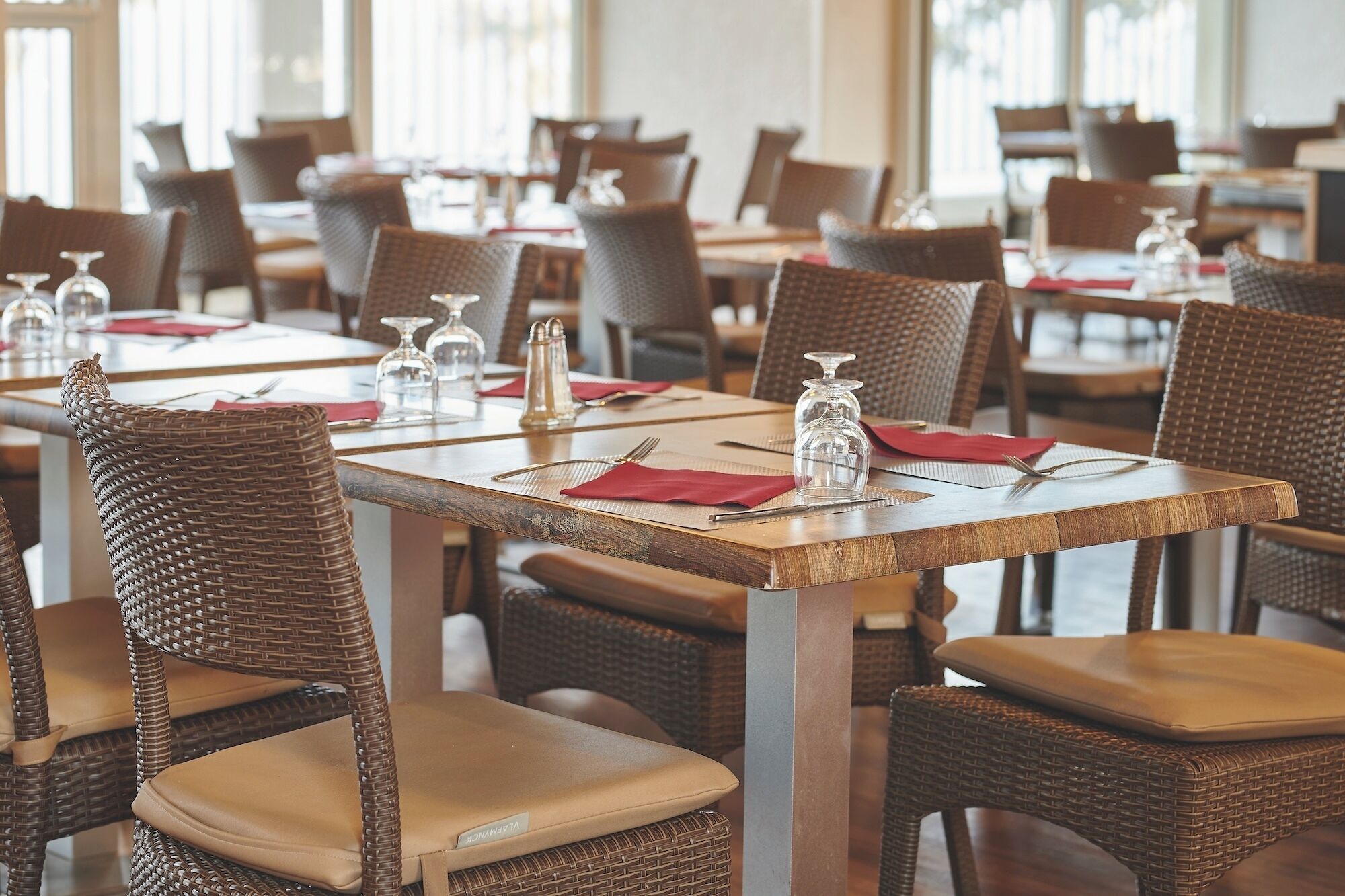 A restaurant with wicker chairs and tables, each set with cutlery, napkins, and glassware.