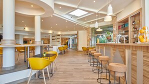 A modern interior with high ceilings, natural light, and a bar area with stools and a variety of beverages. - Club Vacances Bleues Plein Sud (Hyères)