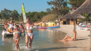 A beach scene with people in swimwear, a sailboat, and beach chairs. - Club Vacances Bleues Plein Sud (Hyères)