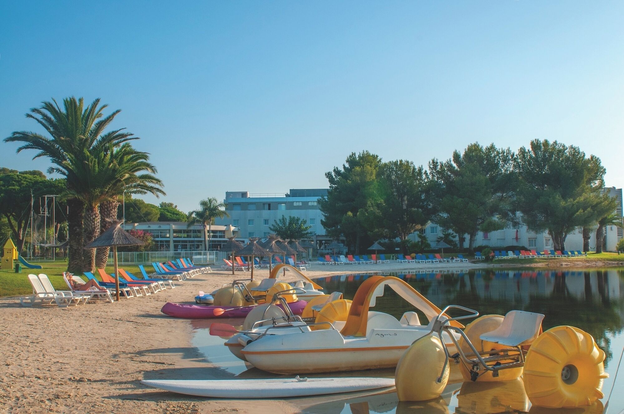 A beach with paddle boats, lounge chairs, and a calm lake.