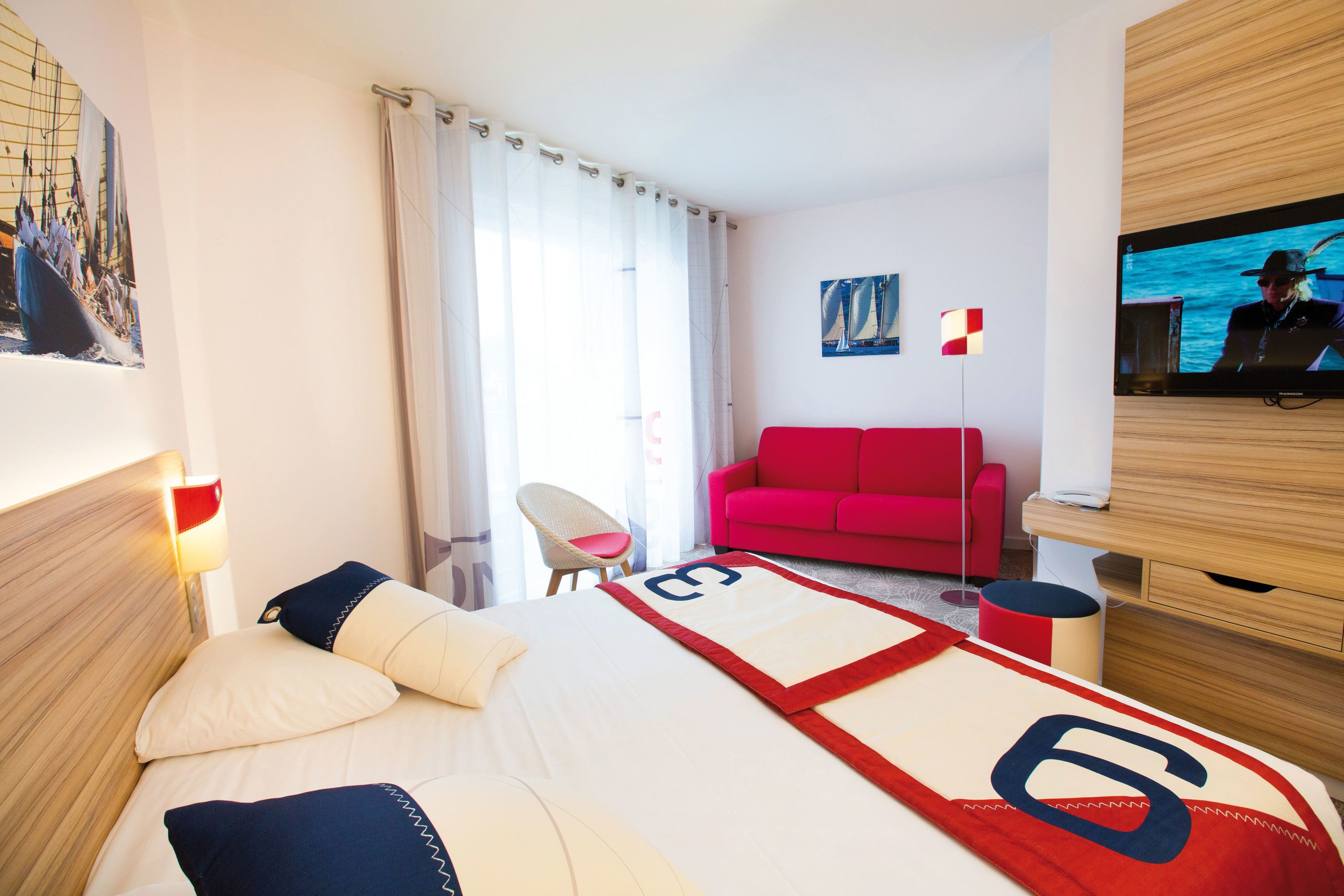 Une chambre d’hôtel avec un lit, un canapé rouge, une télévision et un tableau au mur.