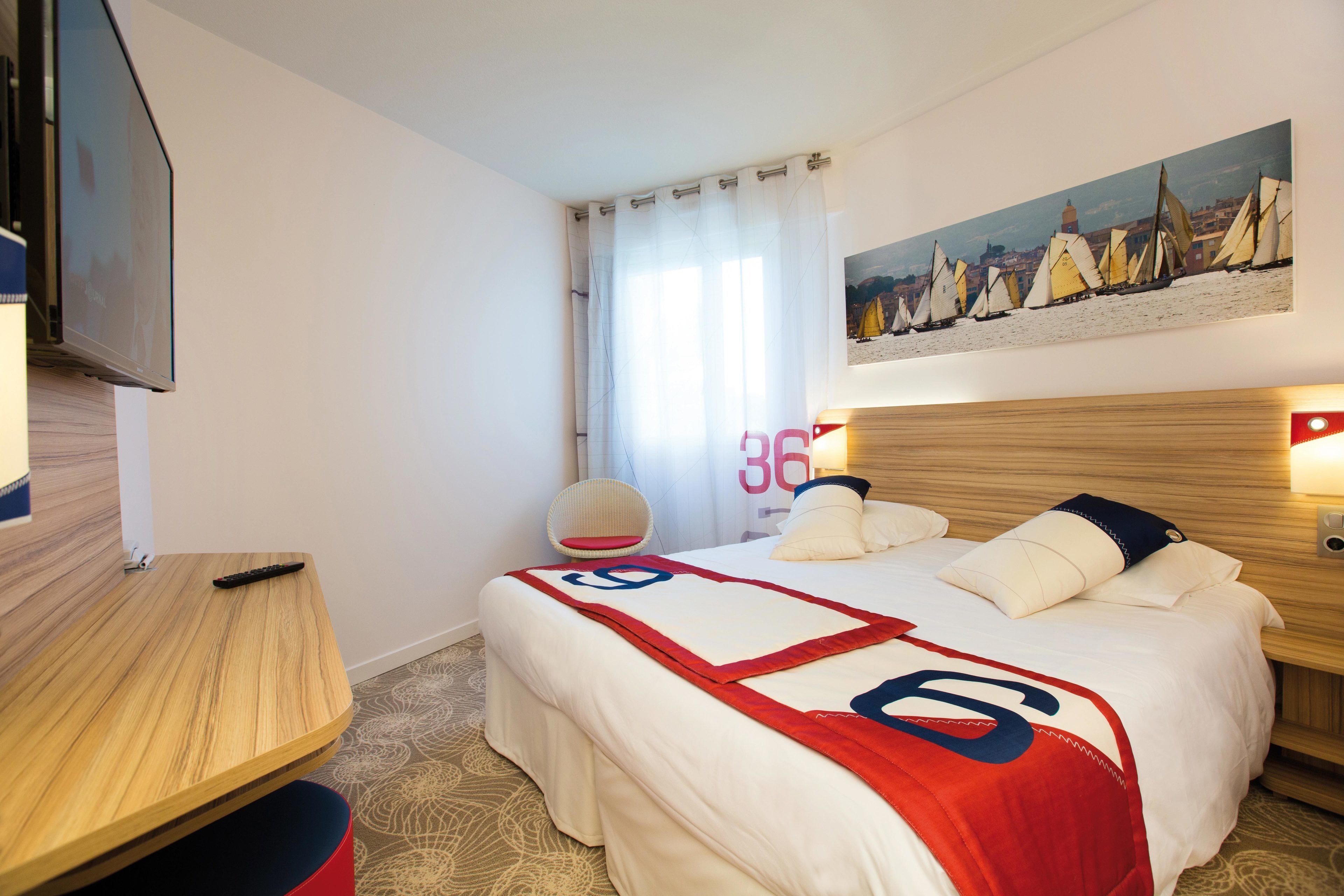 Une chambre d’hôtel avec un lit, une télévision, un bureau et un tableau représentant des voiliers.
