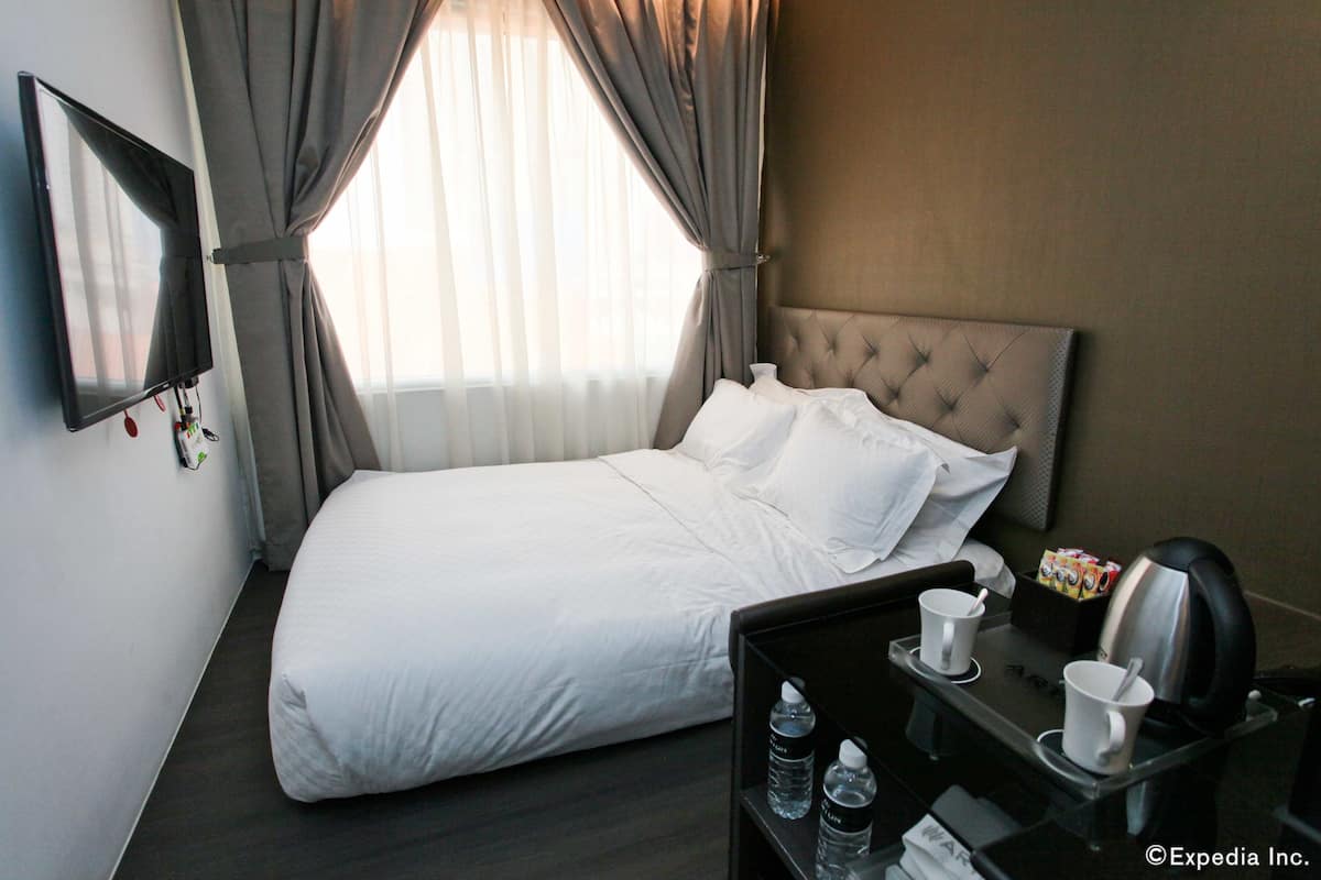Ein Hotelzimmer mit einem ordentlich bezogenen Bett, einem Nachttisch mit Kaffeemaschine und einem Fenster mit Vorhängen.