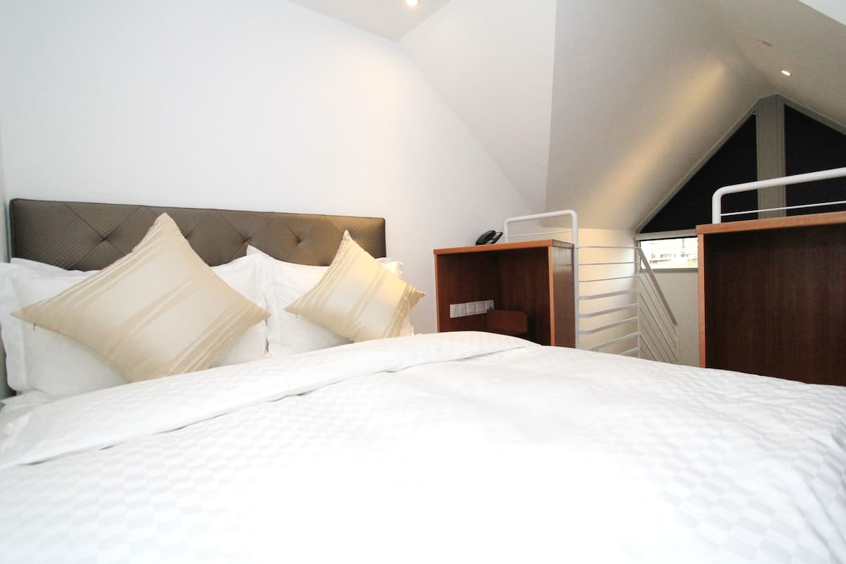 Ein modernes Hotelzimmer mit einem großen Bett, einem Holzkopfende und einem kleinen Nachttisch mit Telefon.