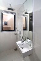 A modern bathroom with a large mirror, a window, and a shower.