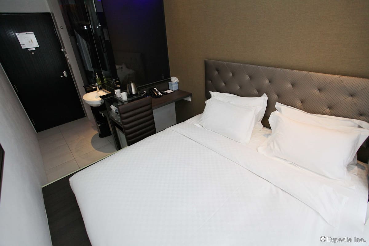 Ein Hotelzimmer mit einem großen Bett, einem Nachttisch mit Spiegel, einem kleinen Schreibtisch und einem Badebereich.