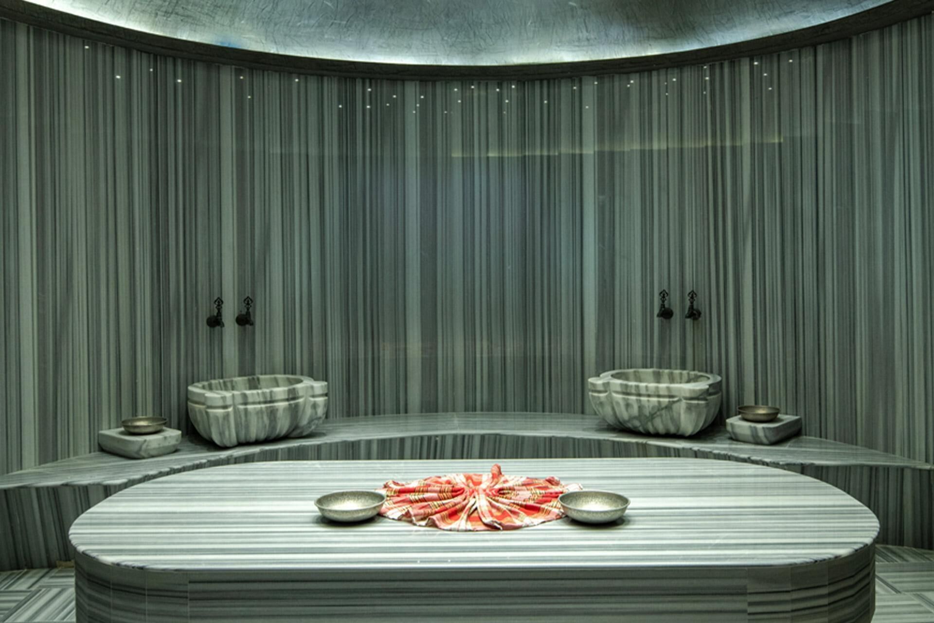 Un cuarto de spa con un banco curvo, dos recipientes y un paño rojo en el suelo.