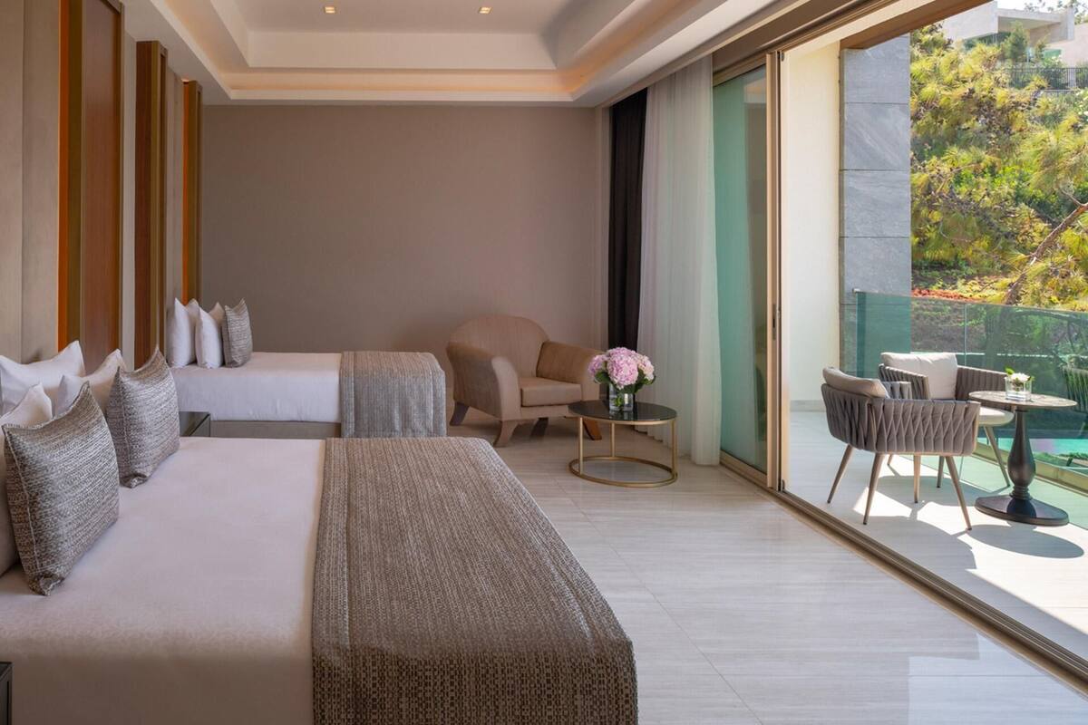 Una habitación de hotel moderna con una cama grande, un sofá, una silla y una pequeña mesa con flores.
