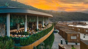 Un restaurante frente al agua con terraza al aire libre, techo curvo y estructuras de madera.