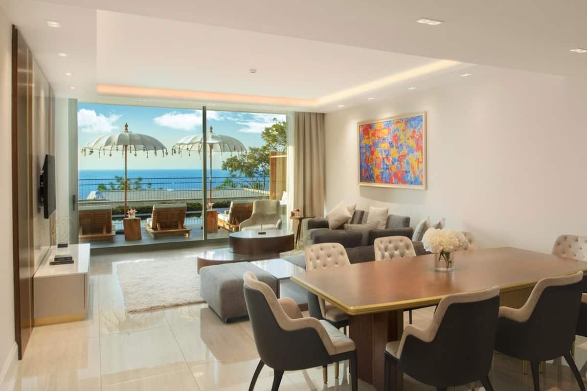 Una sala de estar moderna con un comedor amplio, asientos cómodos, un sofá y vista al océano a través de grandes ventanales.