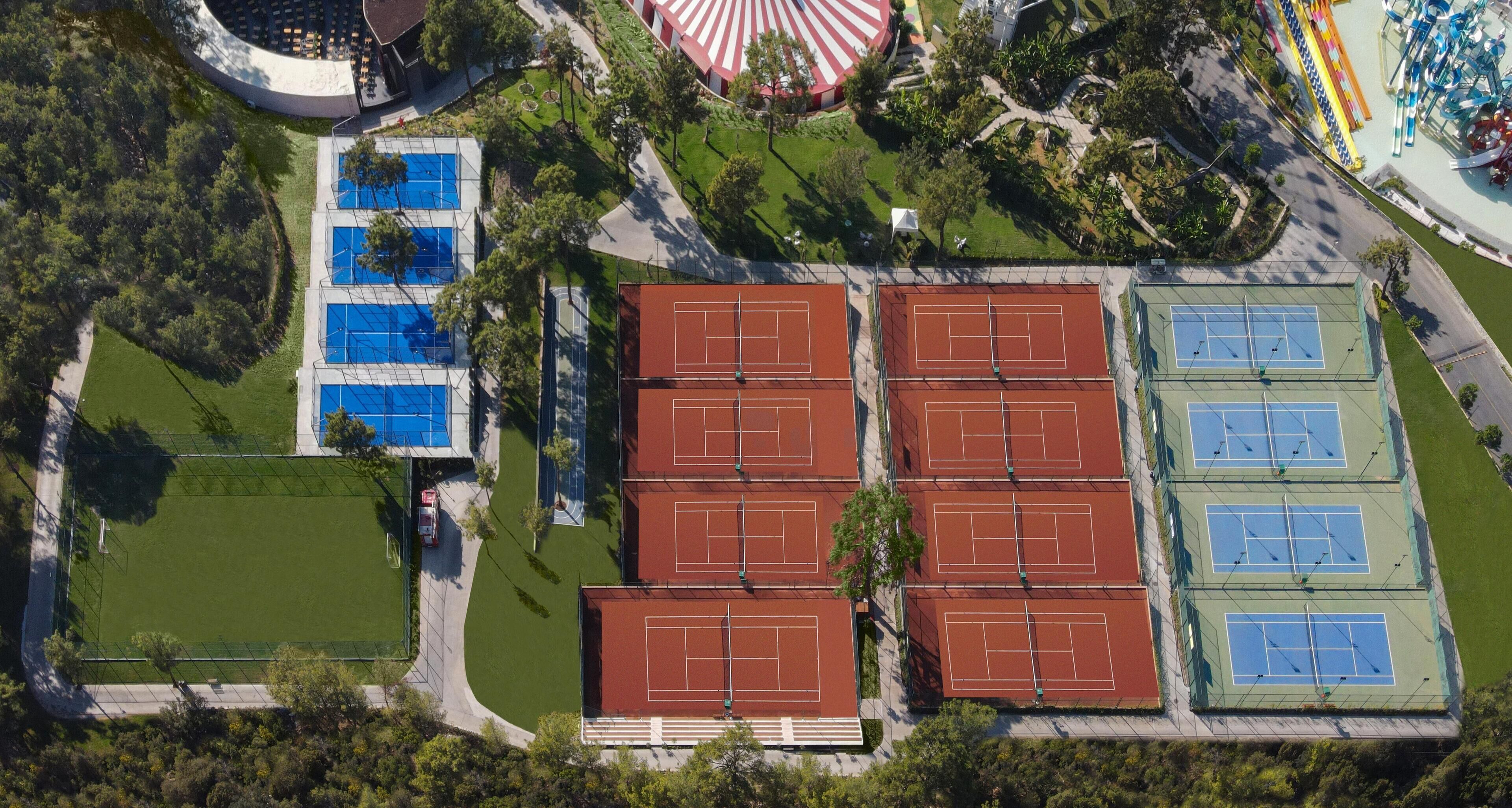 Vista aérea de un complejo deportivo con varias canchas de tenis, una piscina y un carrusel.