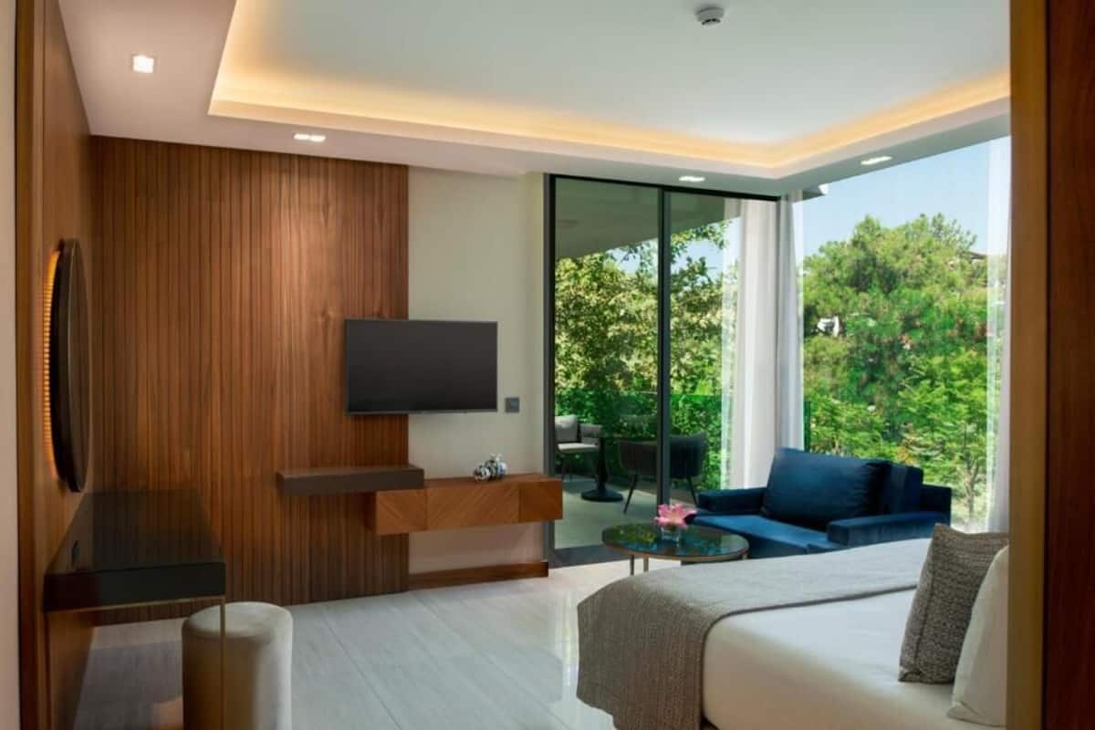 Una habitación moderna con una televisión de pantalla plana, una pared decorativa de madera, un sofá, una mesa de centro y un divisor corredizo de vidrio que da a un espacio exterior.
