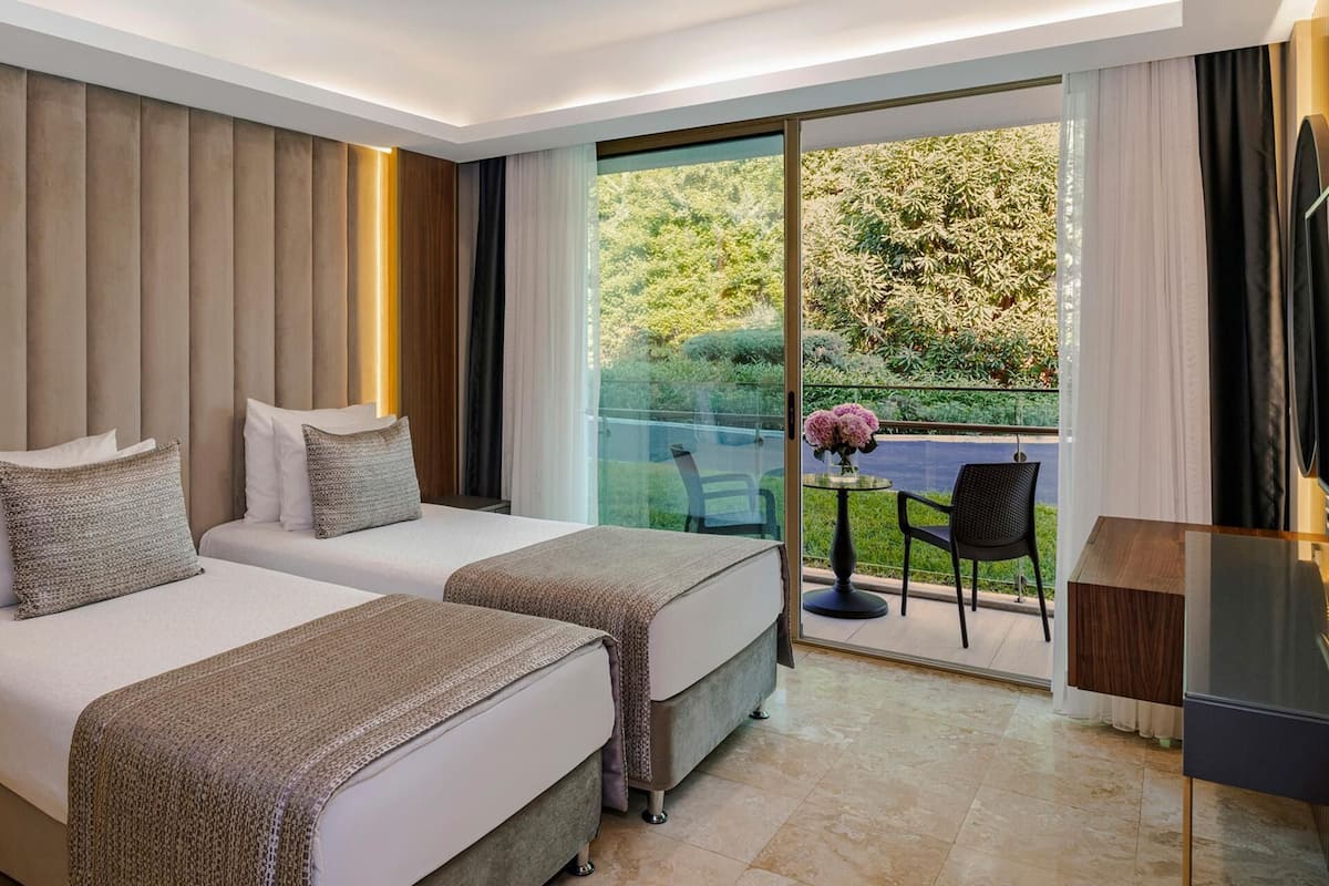 Una habitación de hotel moderna con dos camas, un balcón con mesa y sillas, y un televisor.