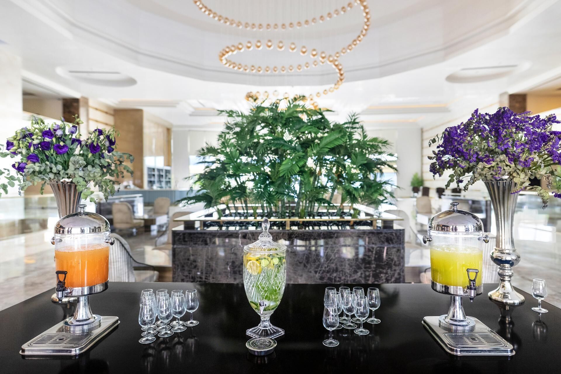 A bar area with two beverage dispensers, a large decorative plant, and multiple wine glasses on a marble table.