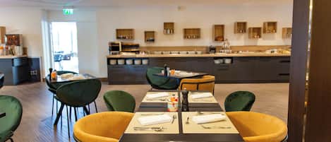 A modern dining area with a long table set for four, surrounded by green and yellow chairs.