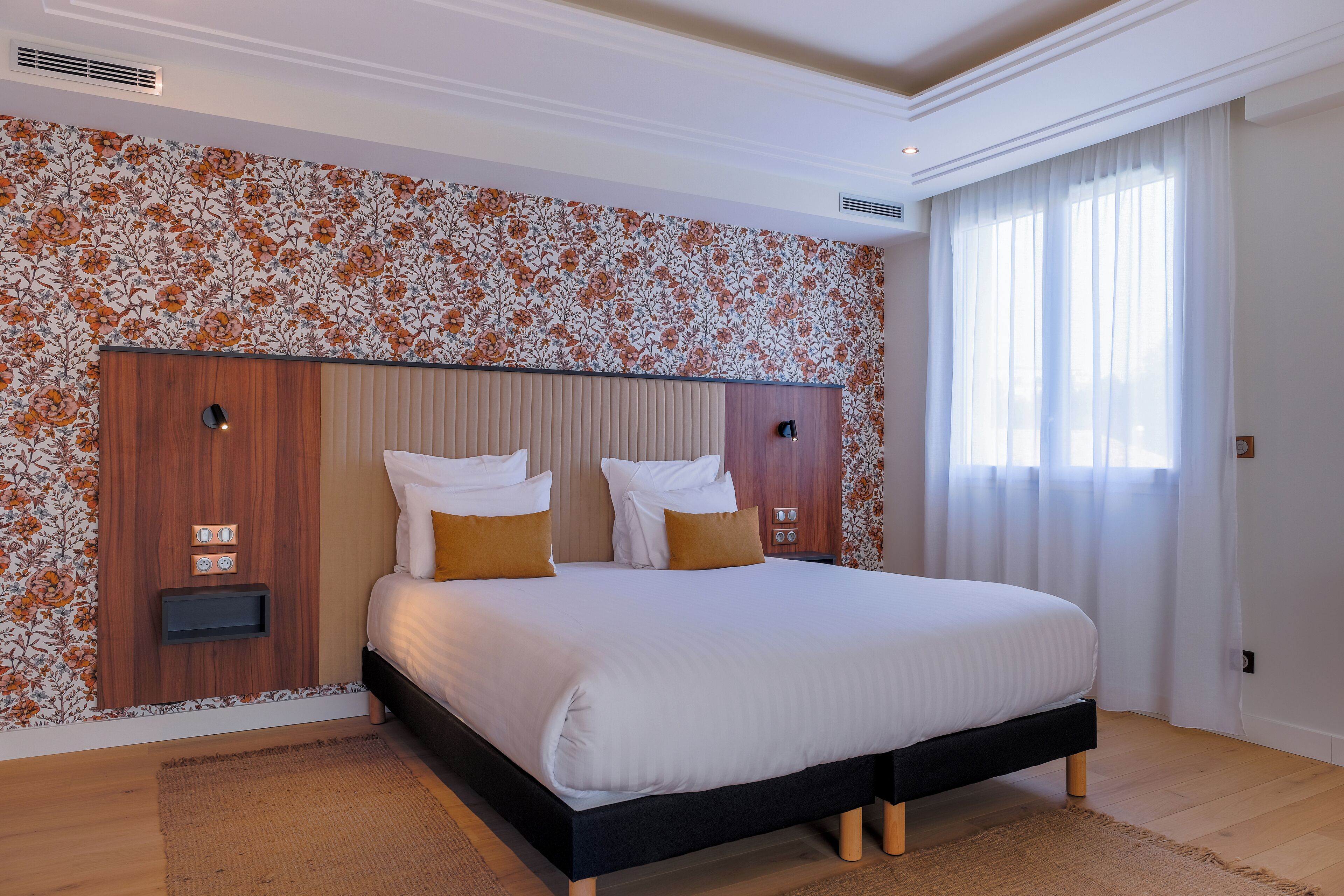 Une chambre moderne avec un grand lit, une tête de lit en bois et un papier peint à motifs floraux.