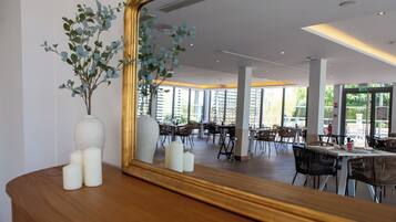 A modern dining area with wooden tables and chairs, a large mirror reflecting the space, and a vase with greenery on a wooden surface.
