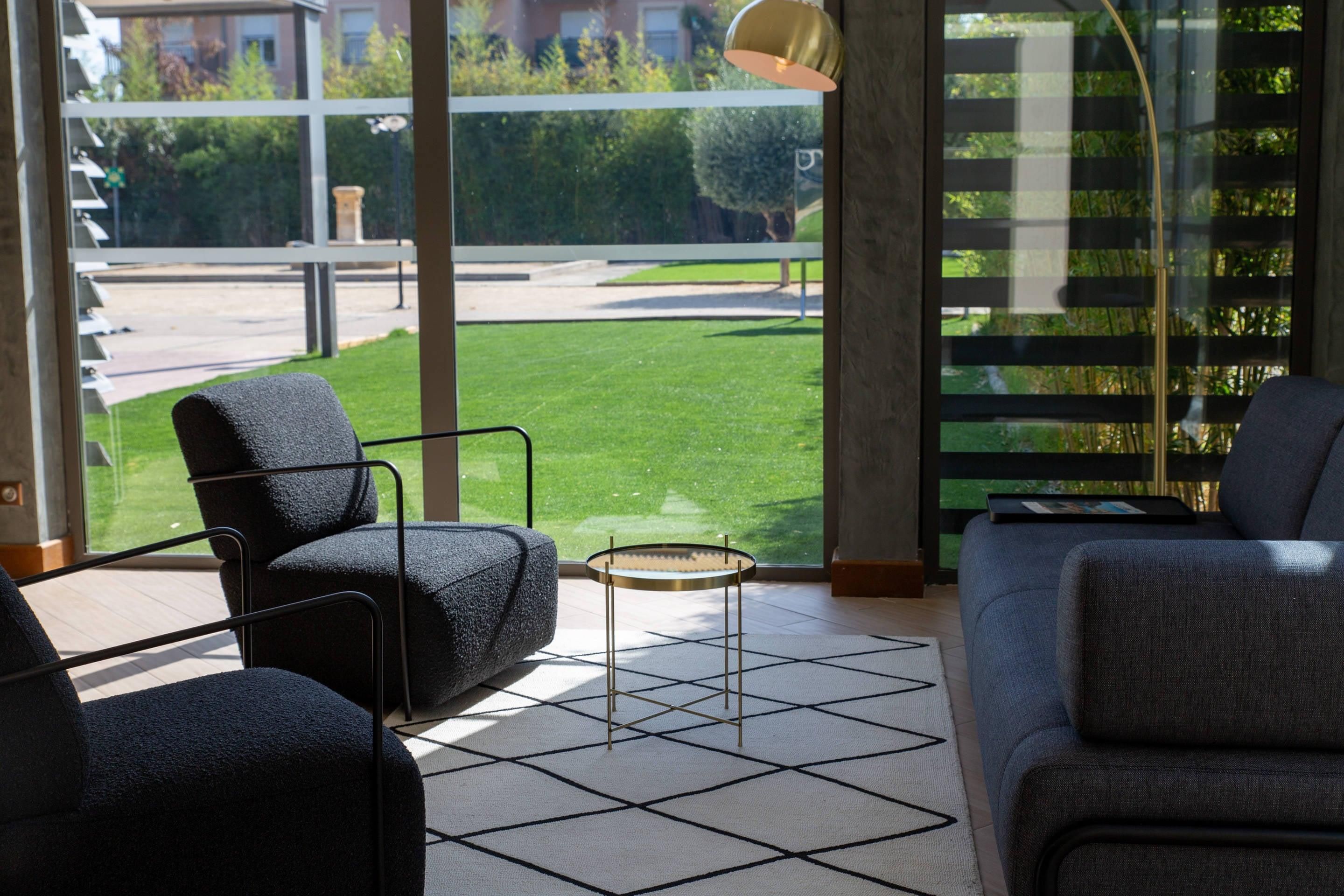 A modern living room with a sofa, armchairs, a coffee table, and a view of a green lawn through large windows.