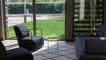 A modern living room with a sofa, armchairs, a coffee table, and a view of a green lawn through large windows.