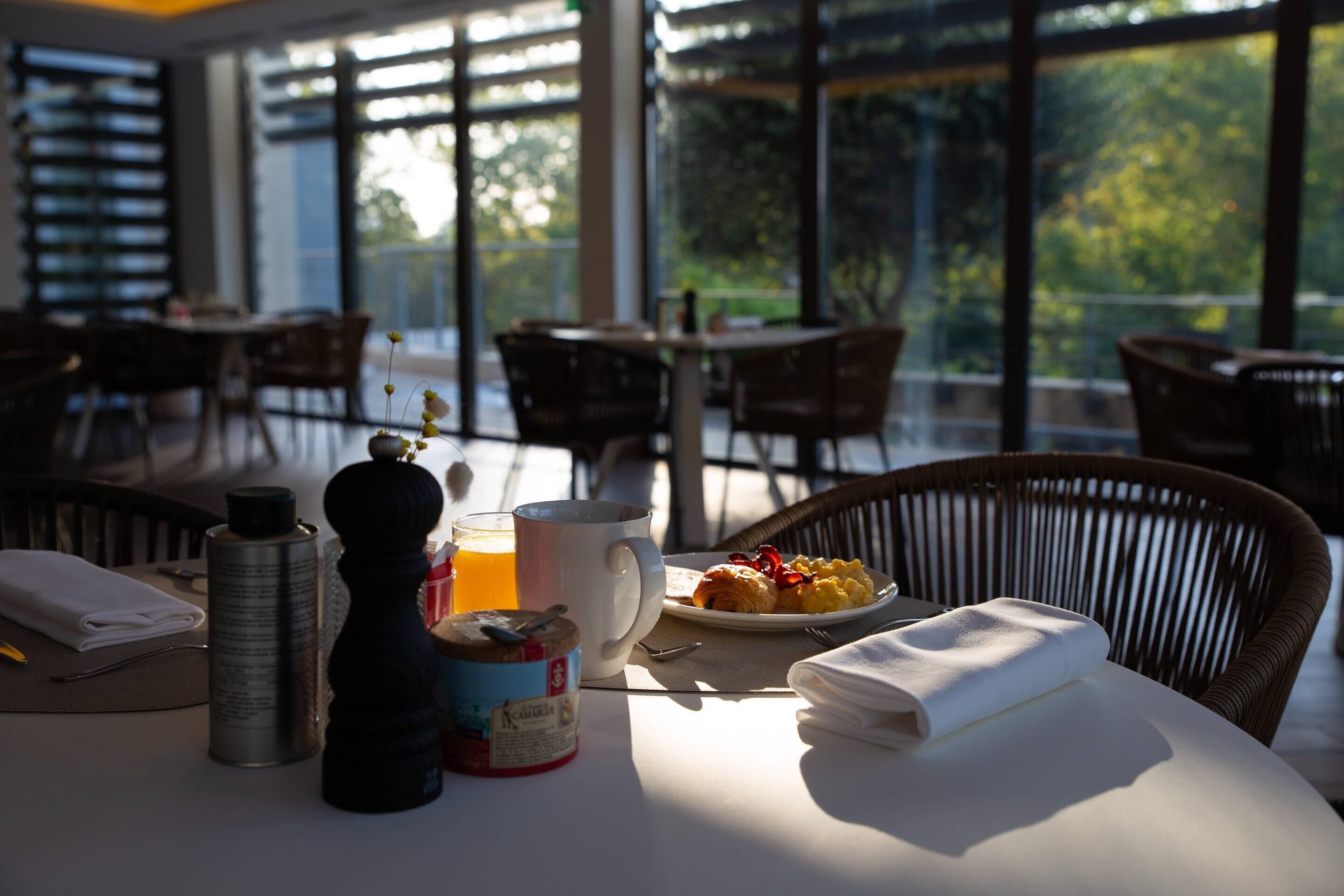 A breakfast table with a plate of eggs, toast, and a drink, set in a bright room with large windows.