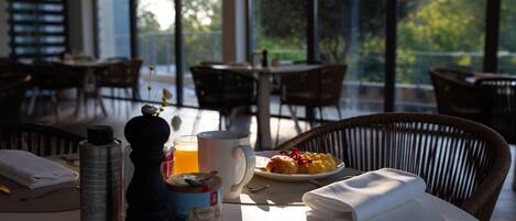 Una mesa de desayuno con huevos, tostadas y una bebida, en una habitación luminosa con ventanas amplias.