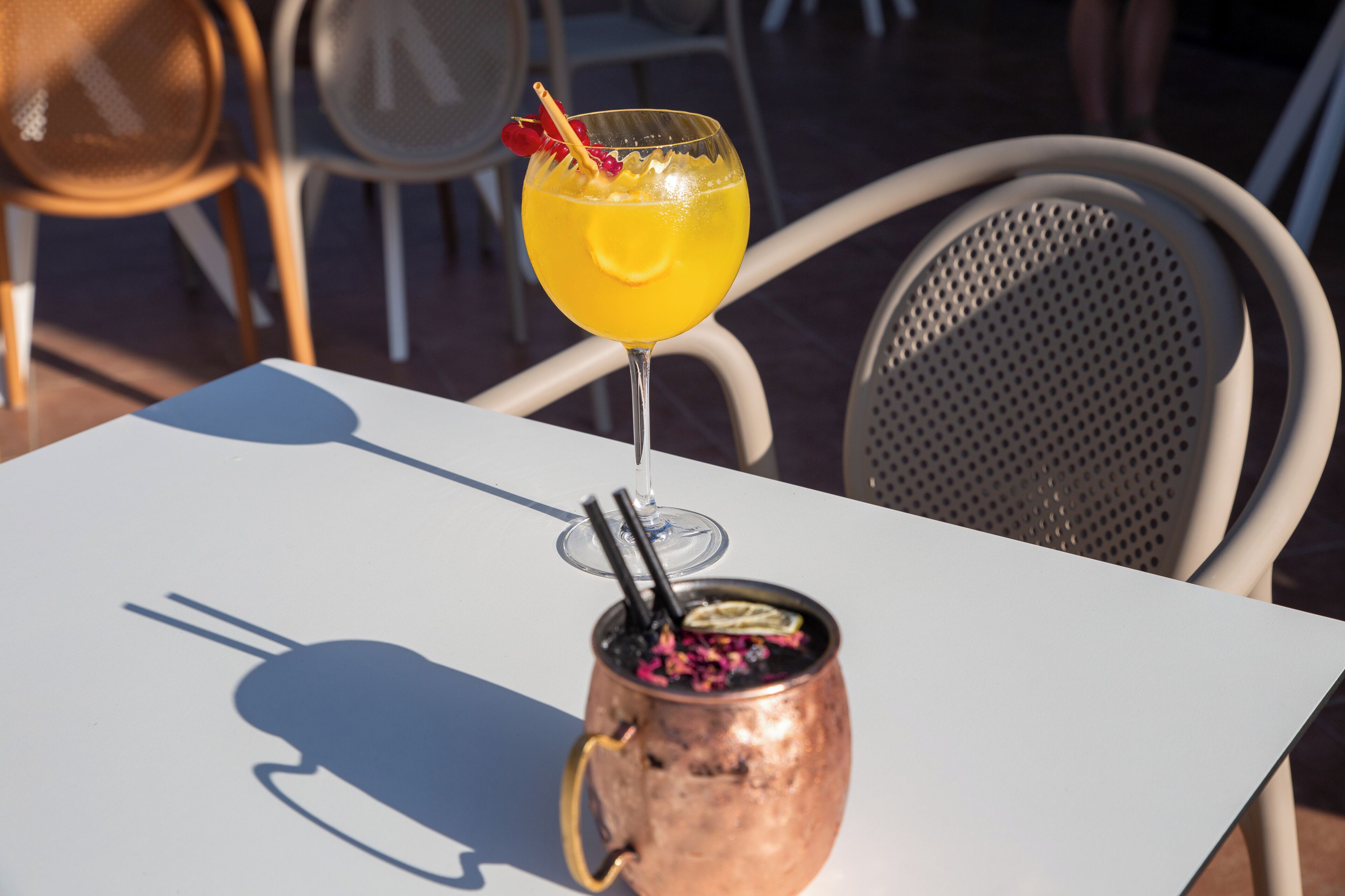 A table with a glass of orange drink and a copper mug with a straw.