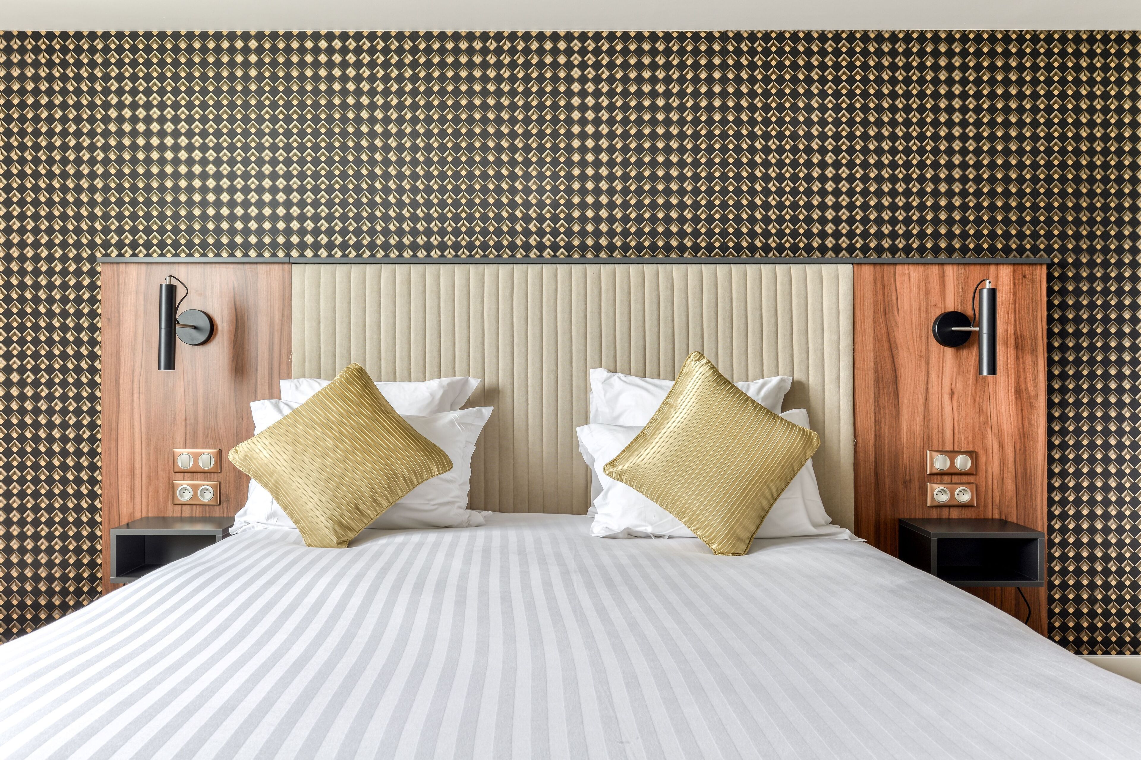 Una habitación de hotel con una cama grande, dos mesitas de noche, un cabecero de madera y un papel pintado decorativo.