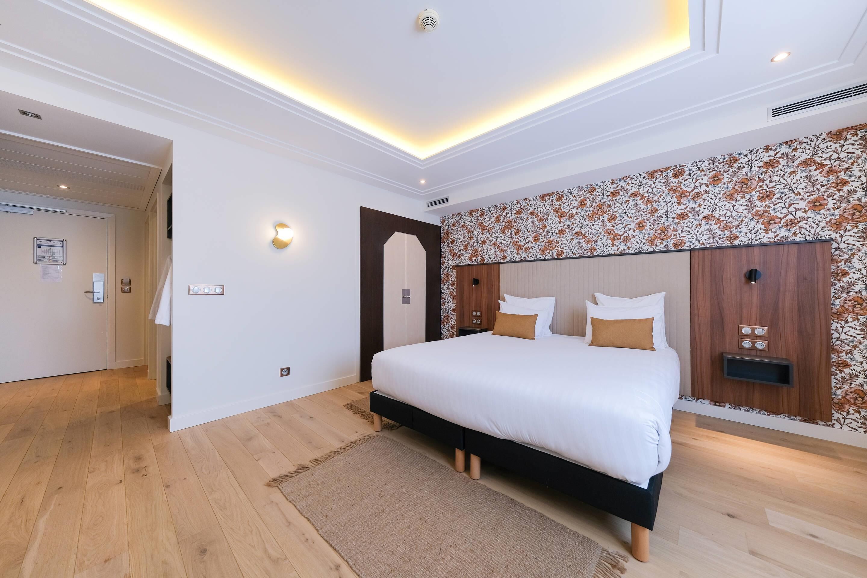 Quarto moderno com cama grande, piso de madeira, parede decorativa e luminária no teto.