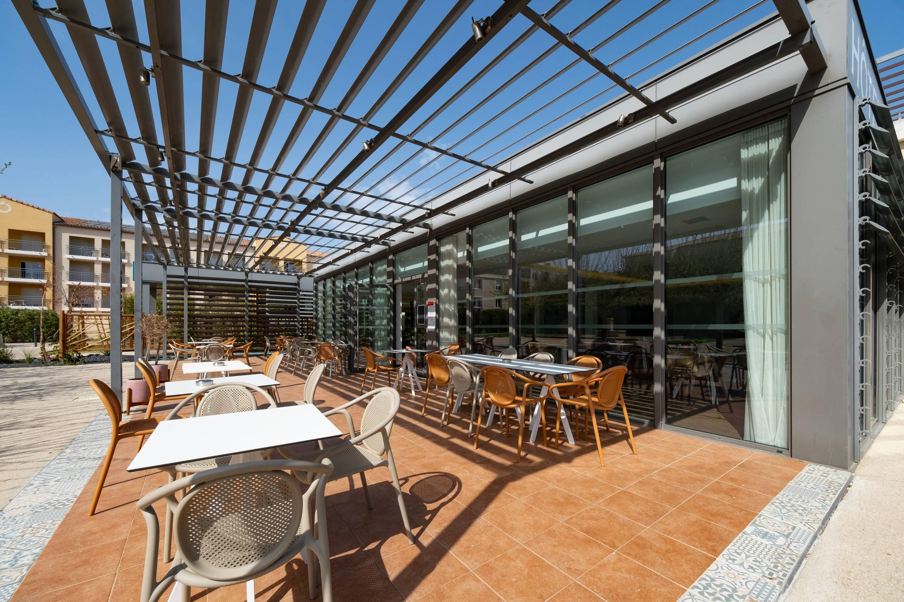 An outdoor patio with tables and chairs, a pergola, and large windows.