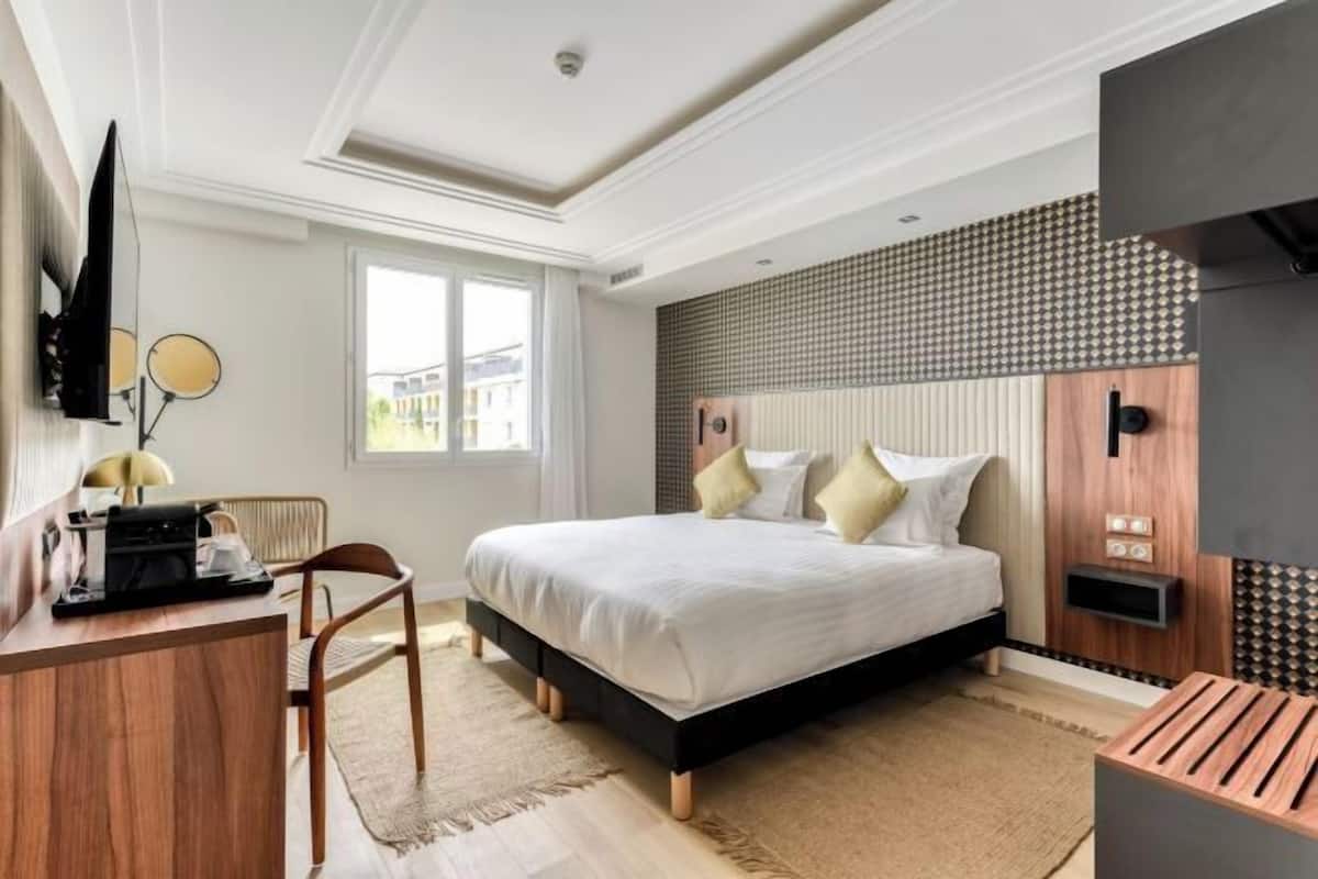 A hotel room with a bed, a desk, a chair, a flat-screen TV, and a window.