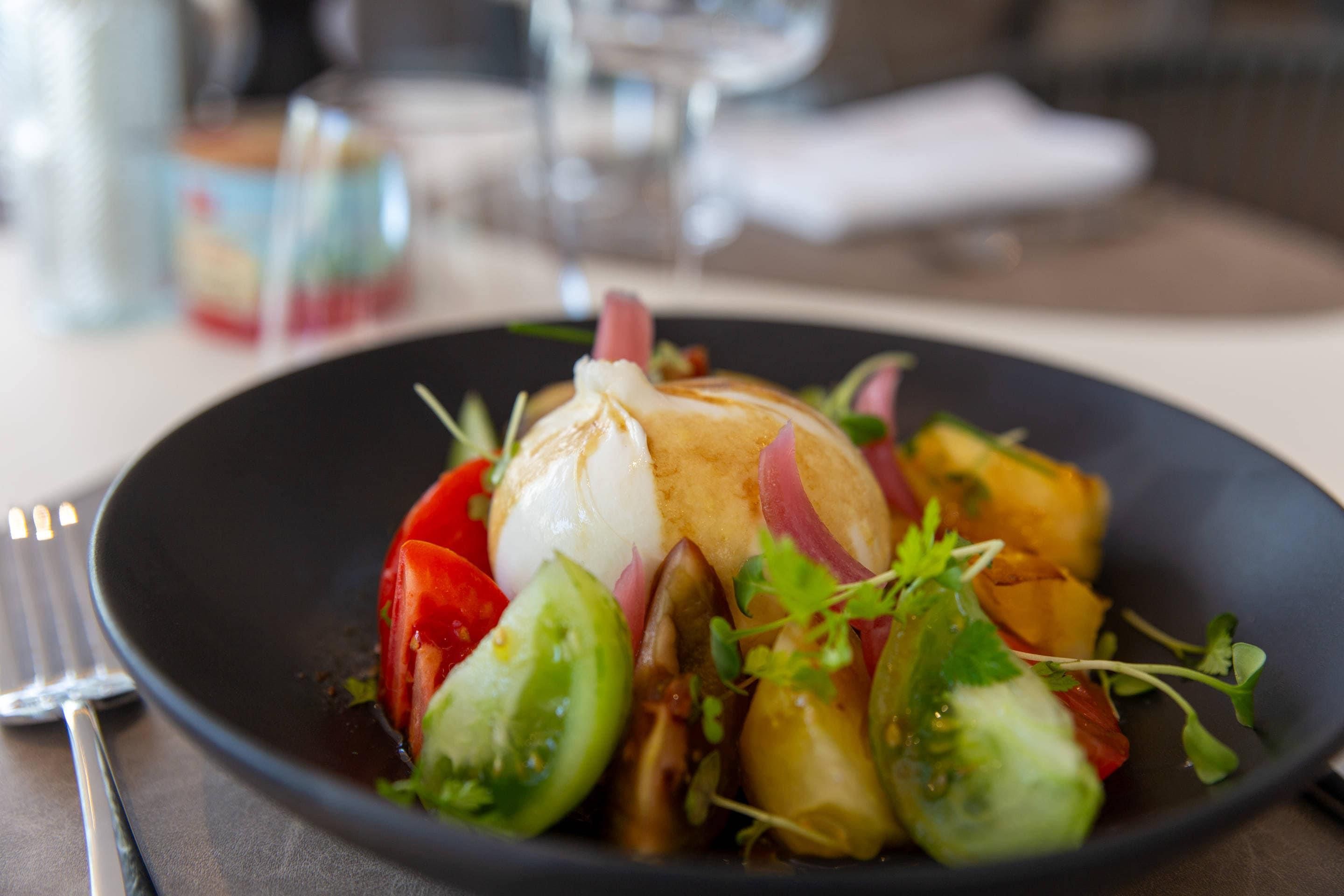 A plate of food with a poached egg, tomatoes, and greens.