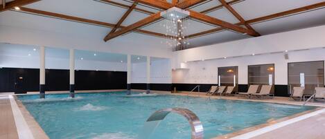An indoor swimming pool with a wooden ceiling and a modern light fixture.