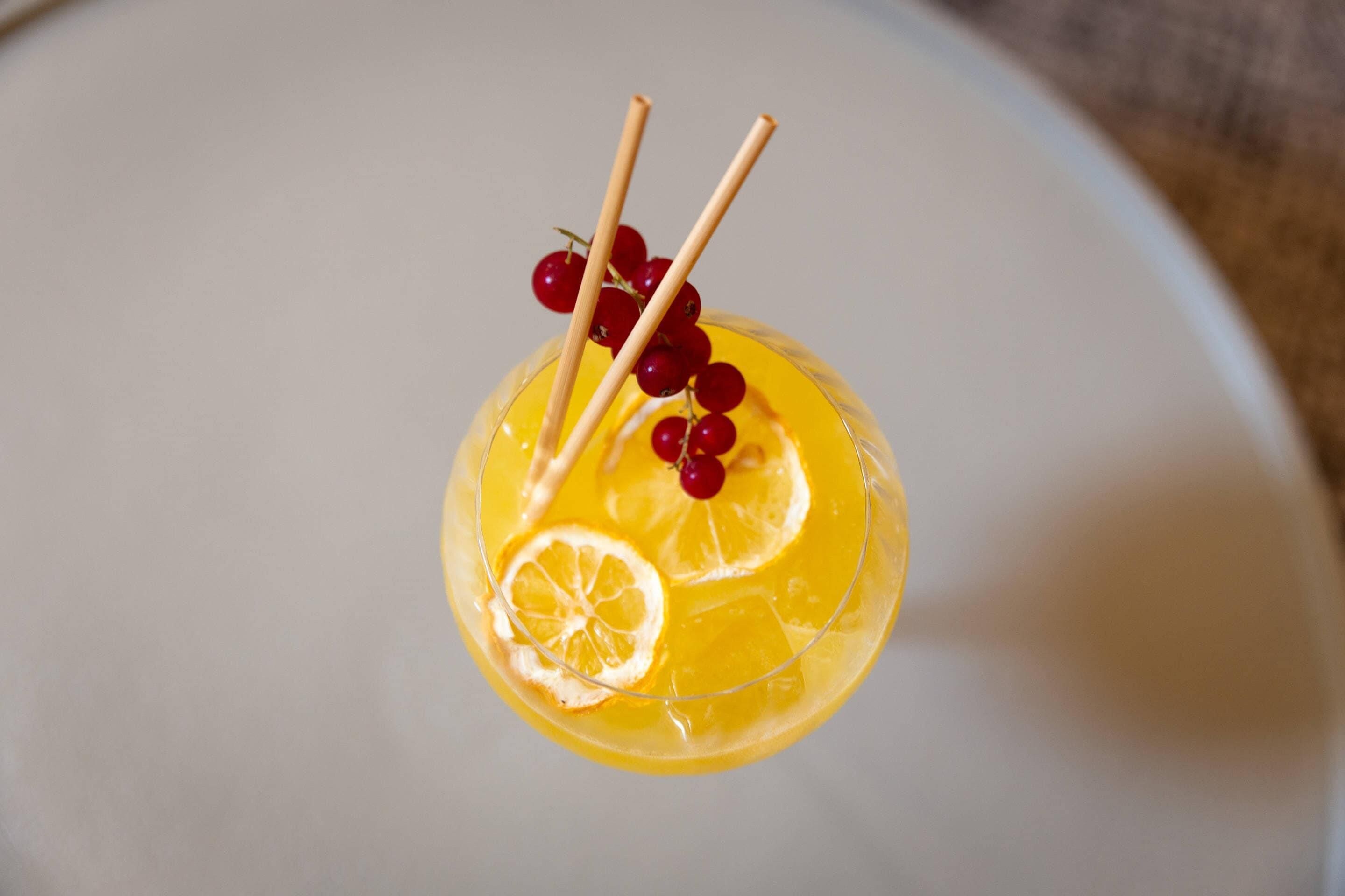 A clear glass with a yellow liquid, garnished with red berries and orange slices.