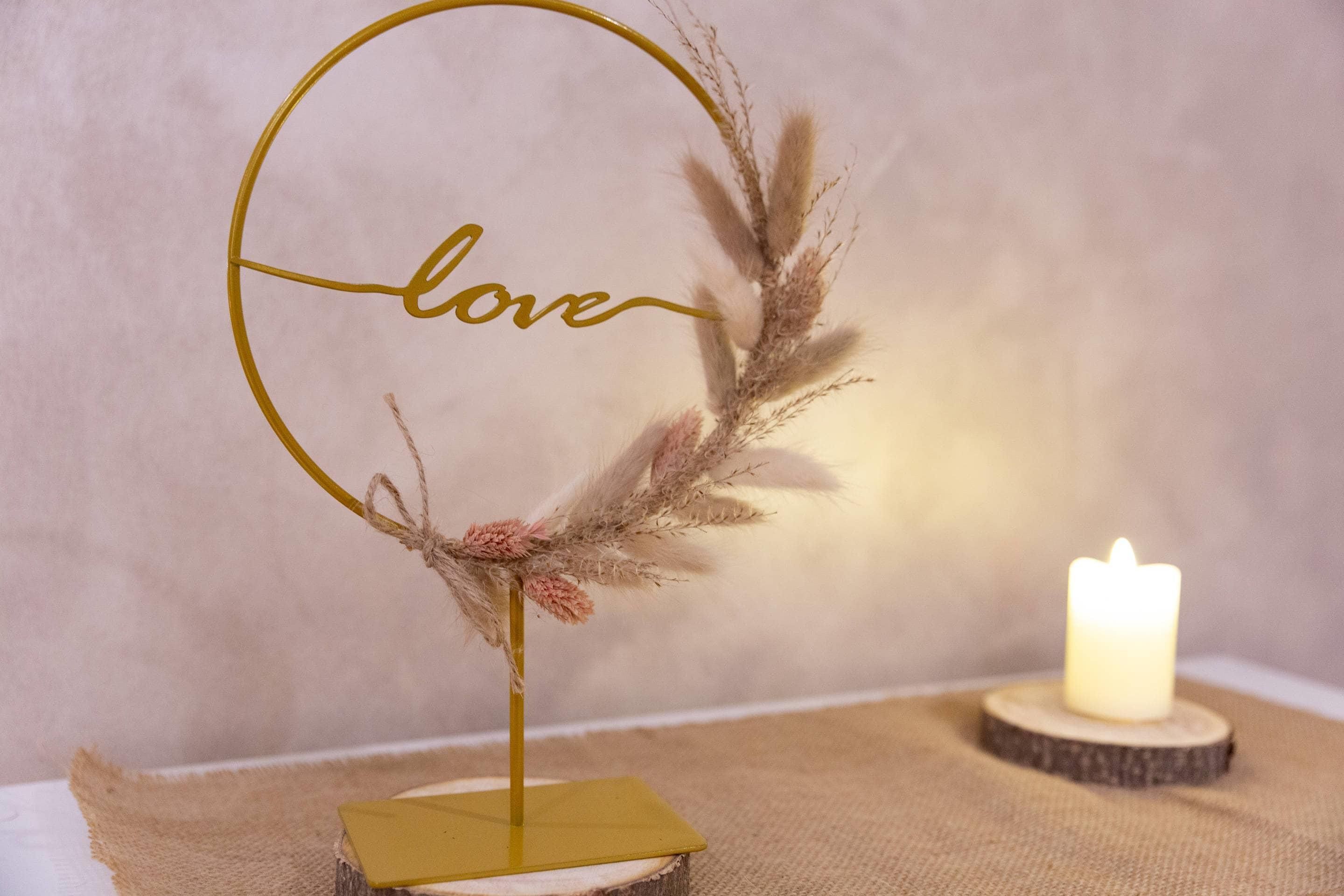 A decorative gold frame with the word 'love' and a candle on a wooden base.