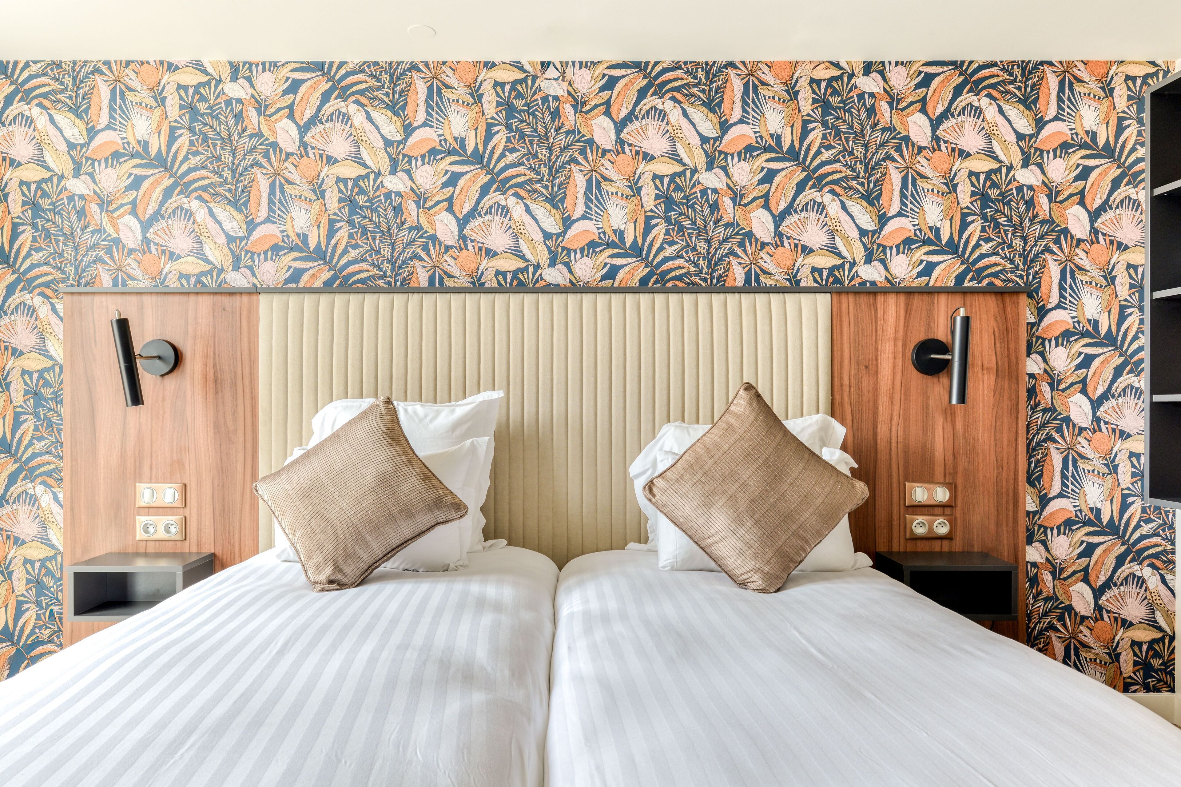 A double bed with a striped bedspread, two bedside tables with clocks, and a floral wallpaper pattern.