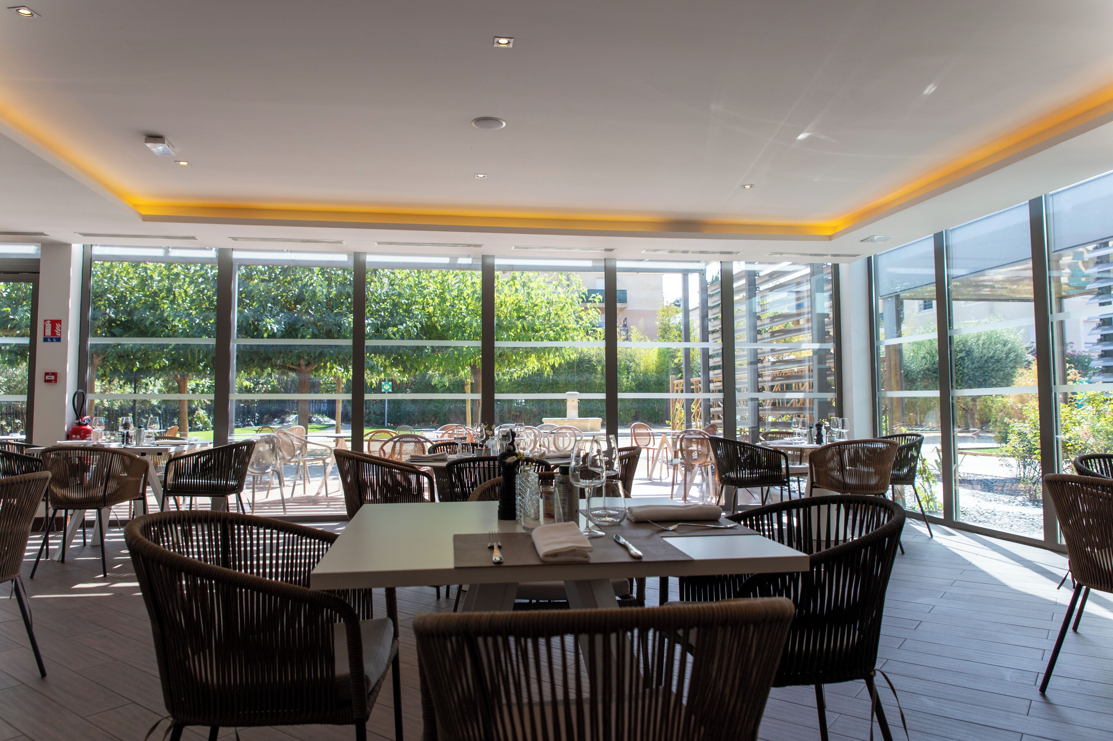 A restaurant with large windows, wicker chairs, and tables set for dining.