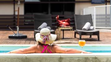 A person relaxing by a pool with lounge chairs and a table in the background.