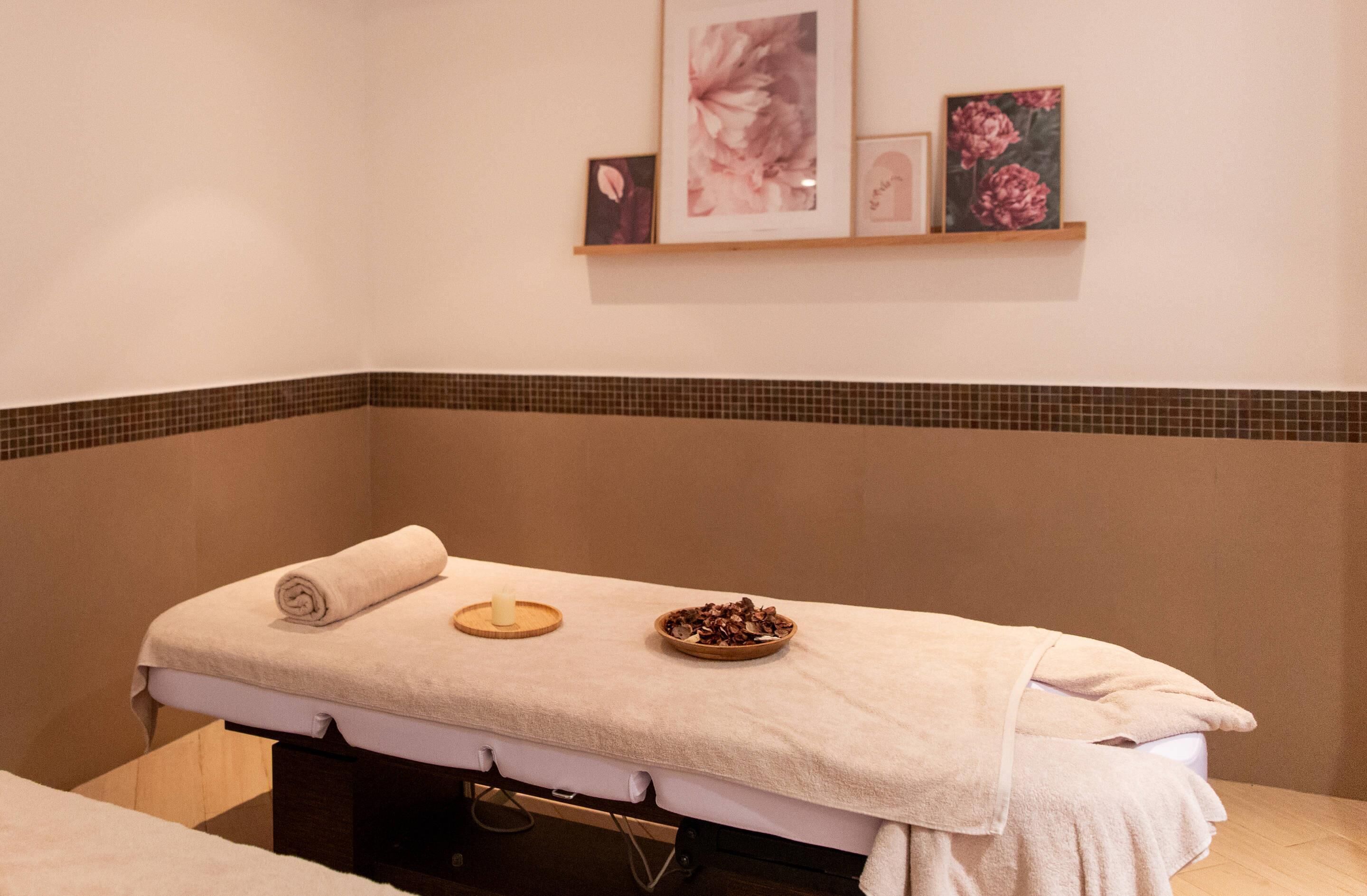 Ein Massagetisch mit Handtuch, eine Schale mit getrockneten Blüten und eine Kerze in einem Wellnessraum.