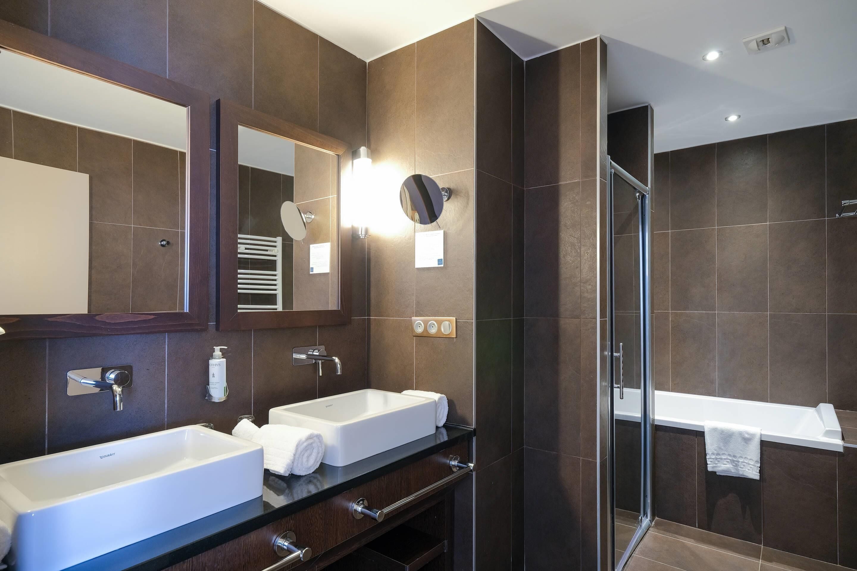 Une salle de bain moderne avec deux lavabos, un grand miroir et une douche à l’italienne.