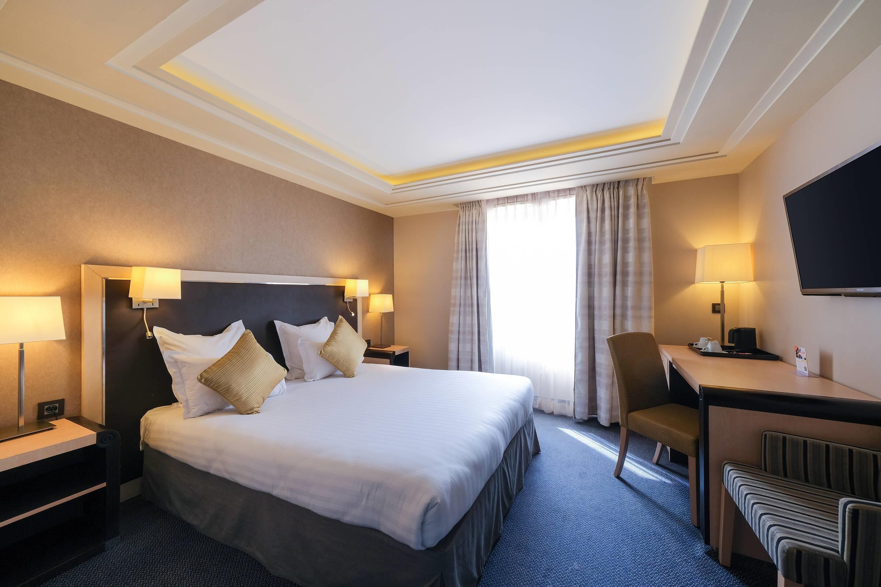 Ein Hotelzimmer mit einem großen Bett, Nachttischen, einem Schreibtisch, einem Sessel und einem Fernseher.