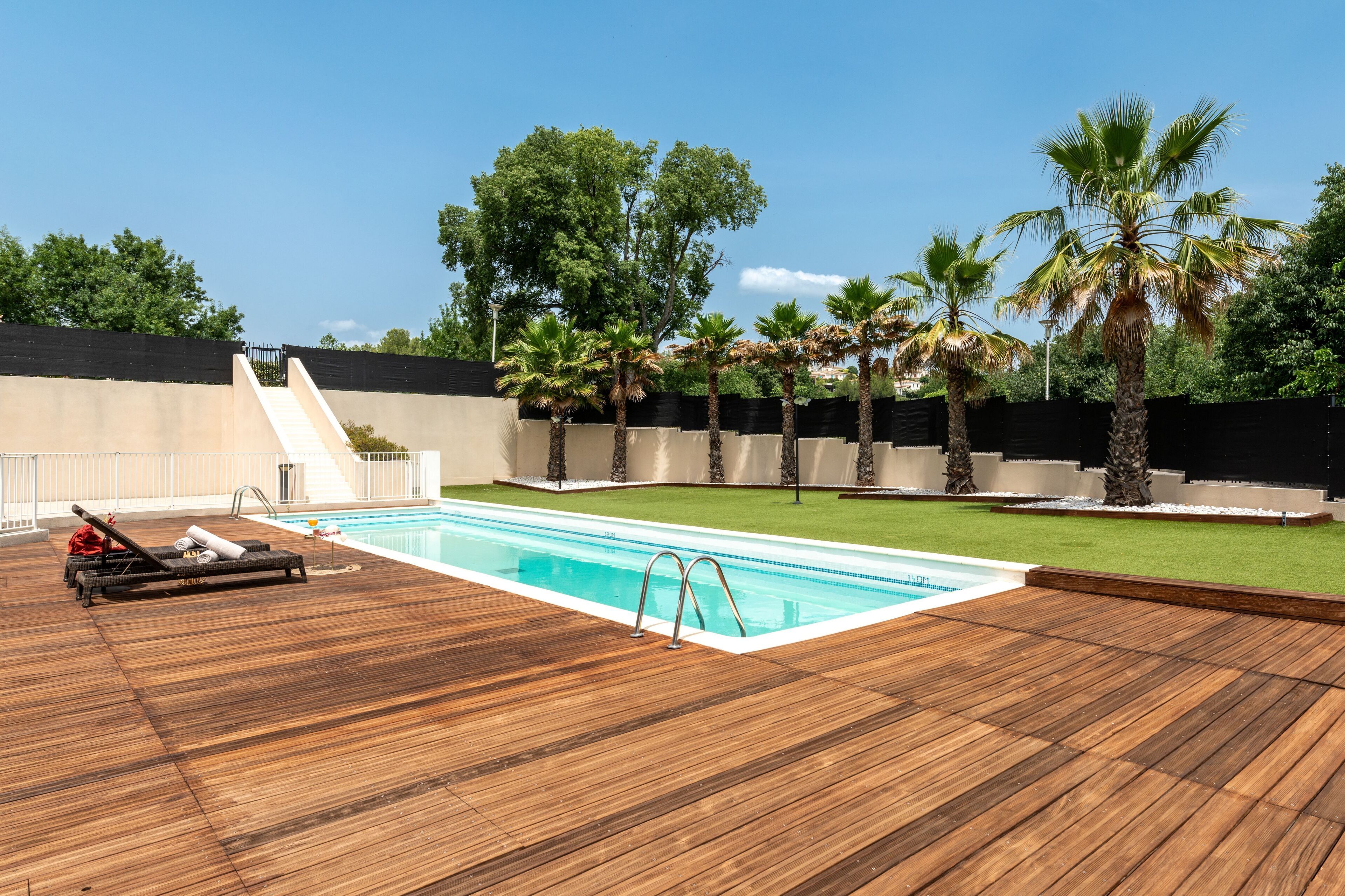 Eine Holzterrasse mit Pool, Palmen und einer Rasenfläche.