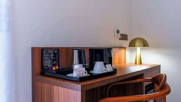 Une chambre d’hôtel avec un bureau en bois, une machine à café, une tasse de café, une lampe et un menu encadré.