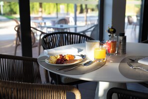 Uma mesa de jantar com itens de café da manhã, um copo de suco de laranja e uma garrafa de água.