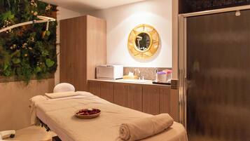 Een wellnessruimte met een massagetafel, een spiegel aan de muur en een klein wastafeltje.
