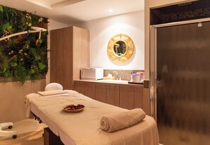 Um espaço de spa com uma mesa de massagem, um espelho fixado na parede e uma pia pequena.