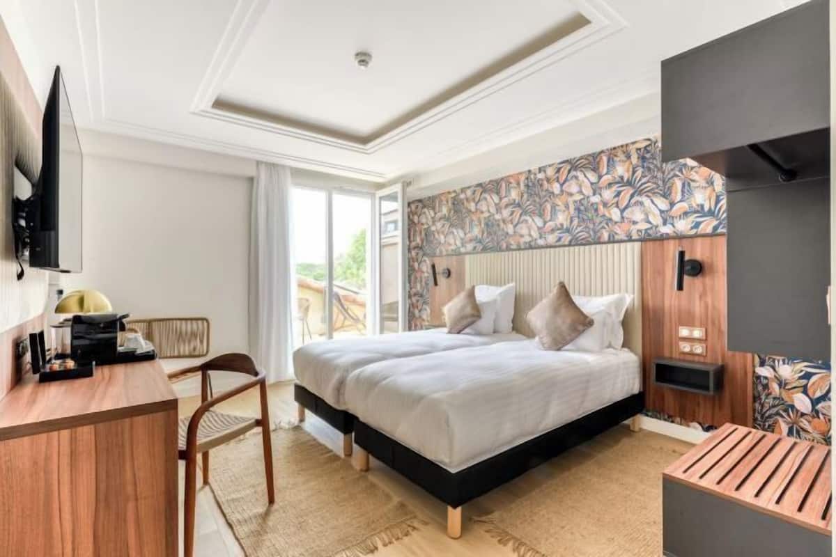 A bedroom with a bed, a desk, a chair, a TV, and a patterned wall.