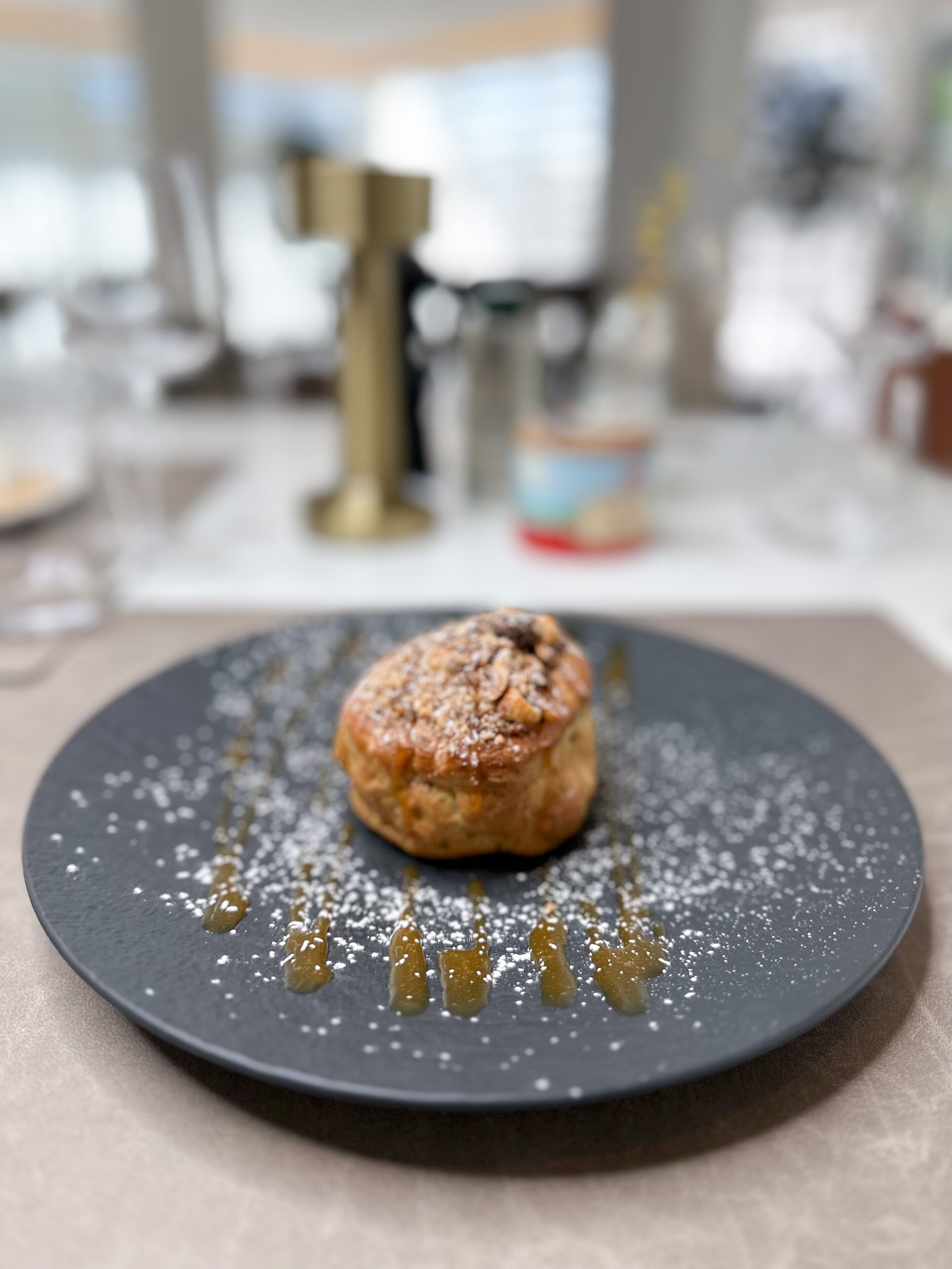 A dessert on a dark plate with a dusting of powdered sugar and syrup drizzle.