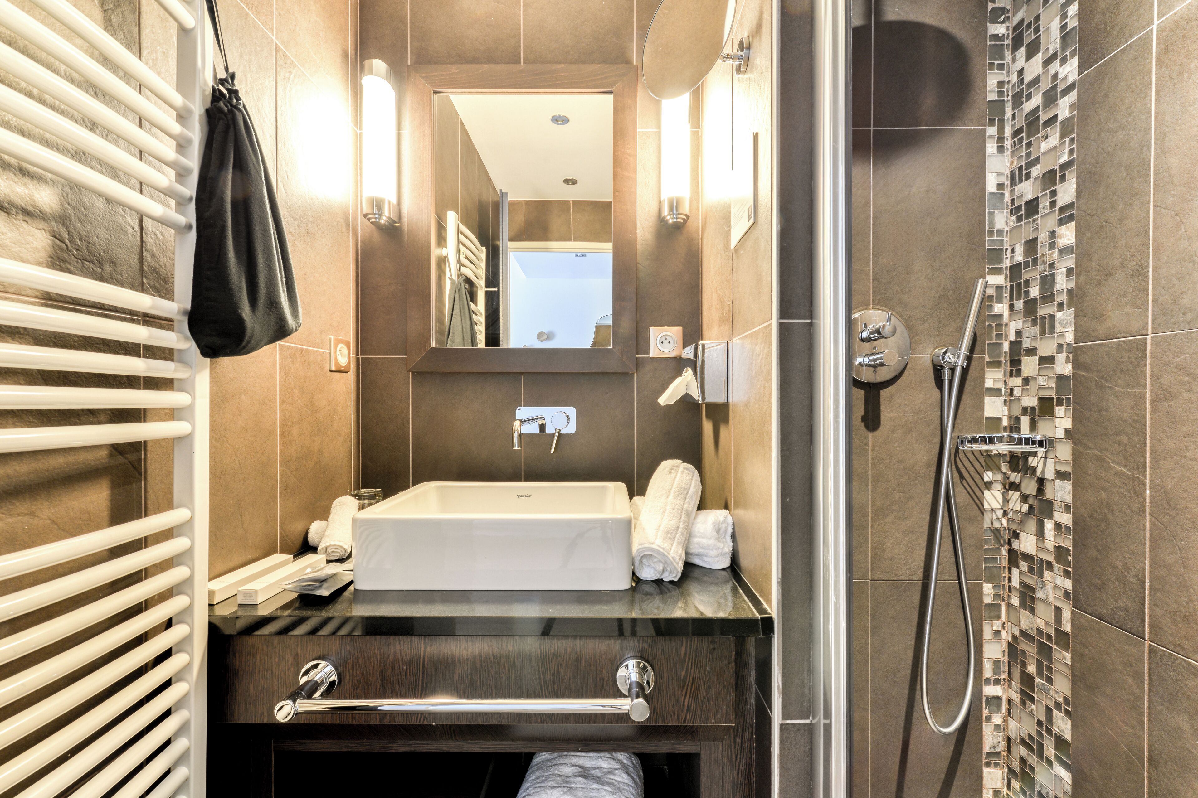 Un baño moderno con un lavamanos grande, espejo, toallero y ducha.