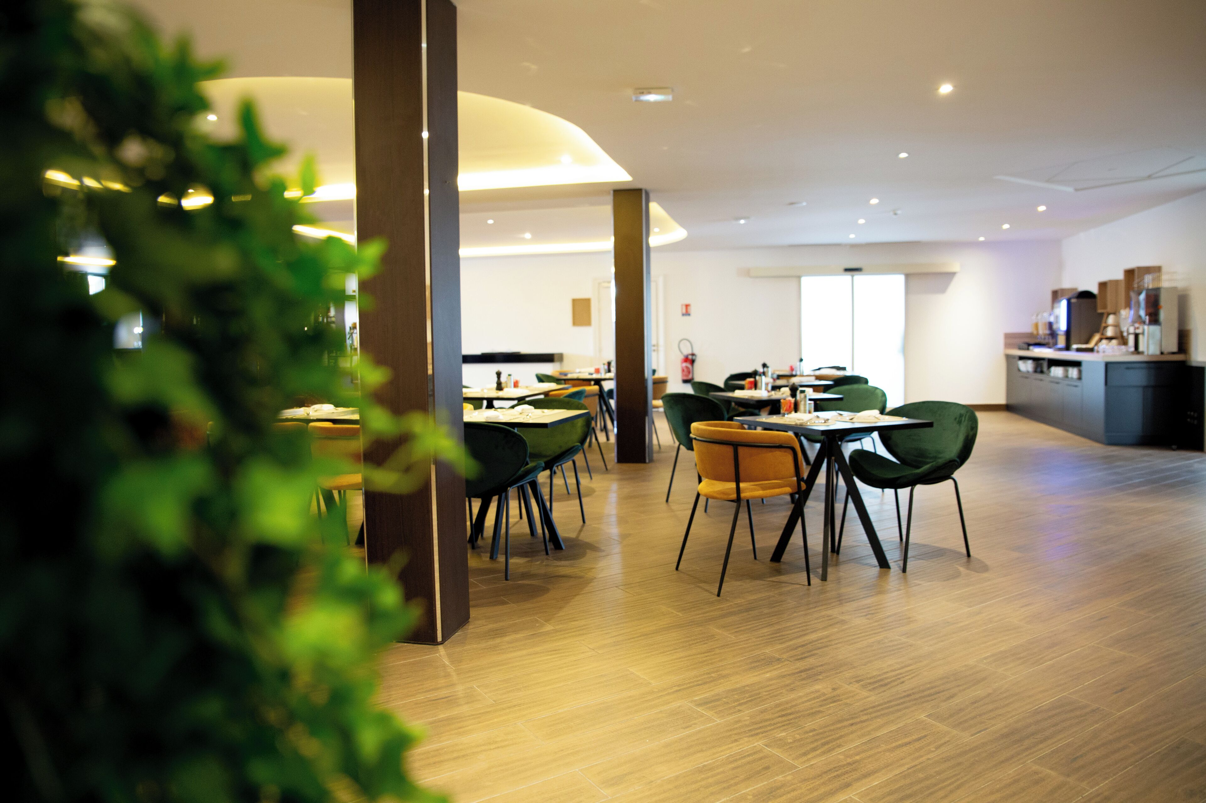 A modern dining area with wooden flooring, green and yellow chairs, and a central table.
