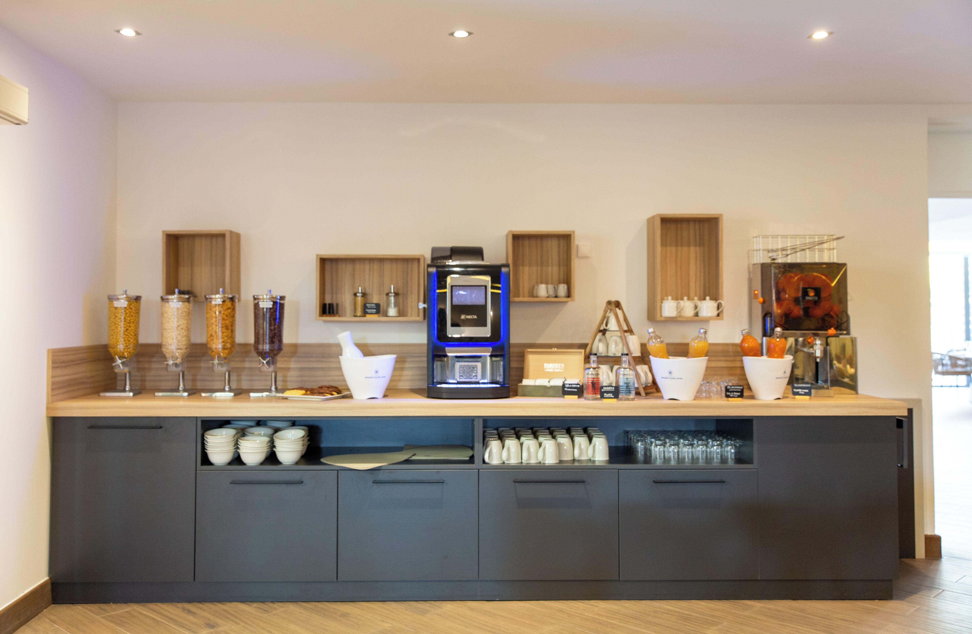 Een moderne ontbijtbar met een koffieapparaat, sapautomaten en ruimte voor bekers en glazen.
